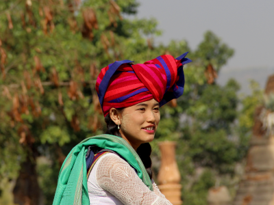 Eine Frau in traditionellen, Bunten Gewändern aus Myanmar. Im Gesicht trägt sich den weißen, landestypischen Sonnenschutz.