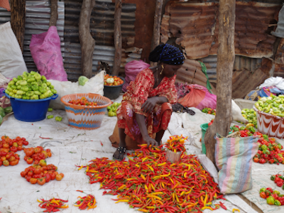 Eine Verkäuferin auf dem Markt in Gambia sortiert Chilis. Sie ist umgeben von Grünen, orangenen, gelben und roten Chilifrüchten.
