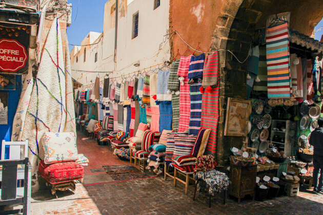 Traditioneller Markt in der Altstadt von Essaouira mit bunten Teppichen, Kissen und marokkanischem Kunsthandwerk. | Gebeco