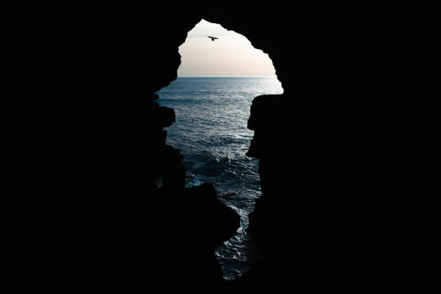 Blick aus der Herkulesgrotte bei Tanger auf den Atlantik bei Sonnenuntergang, mit silhouettierter Felshöhle und fliegender Möwe. | Gebeco