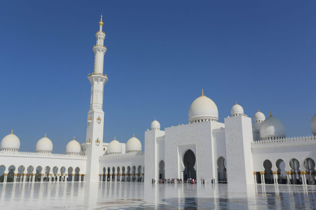 Innenhof der Scheich-Zayid-Moschee in Abu Dhabi mit weißen Kuppeln und Minarett unter blauem Himmel. | Gebeco