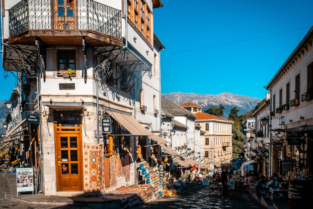 Kopfsteinpflasterstraße in der Altstadt von Gjirokastra, gesäumt von osmanischen Häusern mit Holzbalkonen und traditionellen Läden. | Gebeco