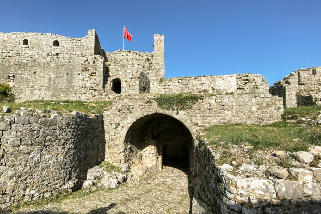 Rozafa-Festung in Shkodra mit Steinmauern und albanischer Flagge auf dem Hügel. | Gebeco