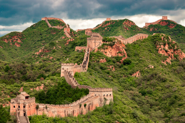 Chinesische Mauer schlängelt sich über grüne Berge unter dramatischem Himmel. | Gebeco