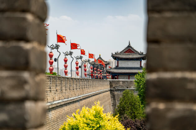 Historische Stadtmauer von Xi’an mit roten Laternen und chinesischen Flaggen bei Tageslicht. | Gebeco