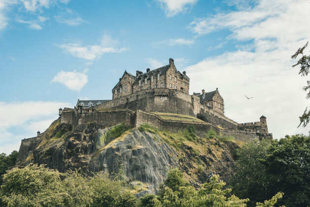 Blick auf das Edinburgh Castle auf dem Castle Rock über der Stadt, umgeben von grünen Bäumen und blauer Himmel. | Gebeco