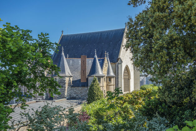 Gotische Schlosskapelle in der Loire-Region Frankreichs, umgeben von grüner Gartenlandschaft und blühender Vegetation im Sommer. | Gebeco