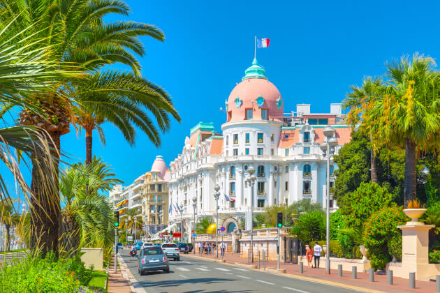 Hotel Negresco an der Promenade des Anglais in Nizza bei Sonnenschein, gesäumt von Palmen und vorbeifahrenden Autos. | Gebeco