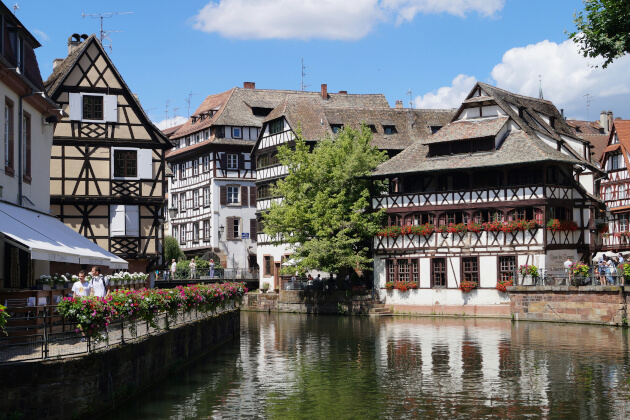 Fachwerkhäuser im Viertel Petite France in Straßburg mit Blumen geschmücktem Kanal bei Sonnenschein. | Gebeco