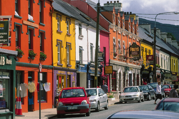 Bunte Häuserzeile in Kenmare mit traditionellen irischen Pubs und Geschäften bei Sonnenschein. | Gebeco