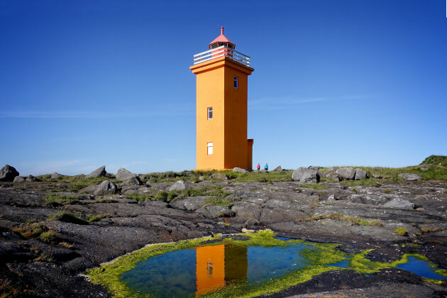 Orangefarbener Hópsnes-Leuchtturm in Grindavík, Island, mit Spiegelung im Wasser bei klarem Himmel. | Gebeco