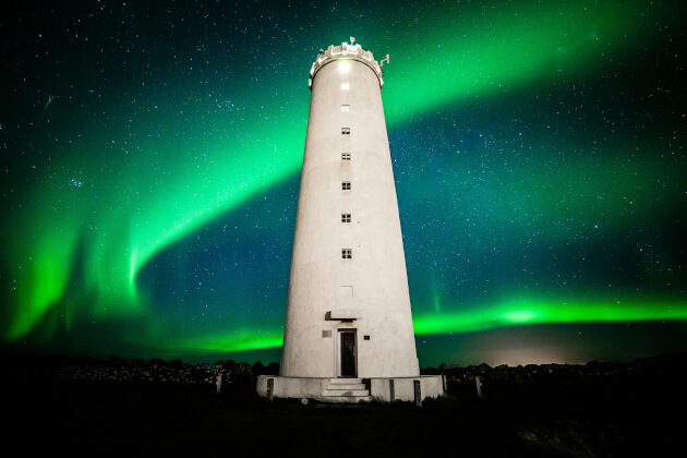 Leuchtturm in Island vor grünen Polarlichtern unter klarem Sternenhimmel. | Gebeco