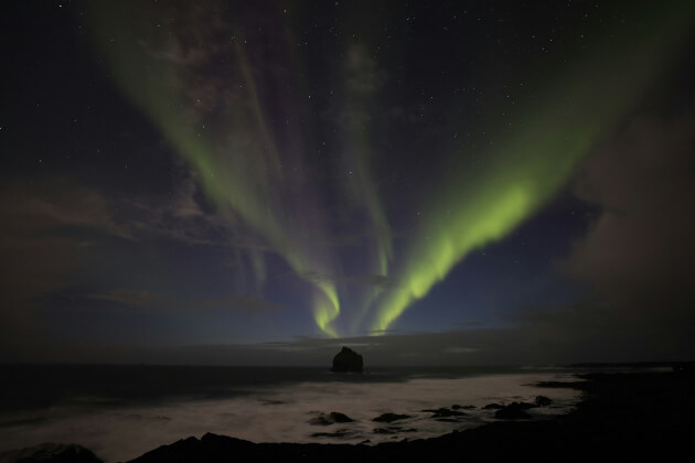 Polarlichter über dem Atlantik in Island bei Nacht mit Felsinsel im Vordergrund. | Gebeco