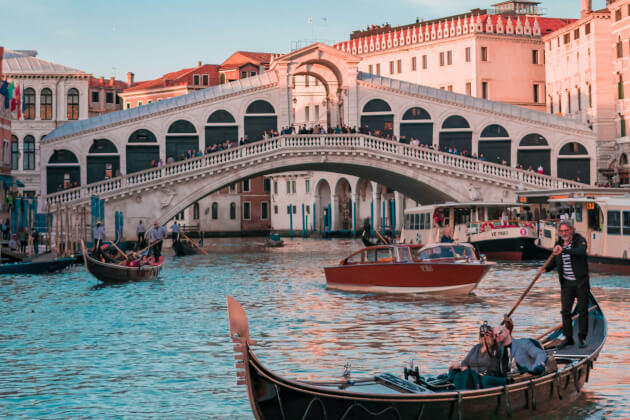 Rialtobrücke in Venedig mit vorbeifahrenden Gondeln auf dem Canal Grande bei Sonnenuntergang. | Gebeco