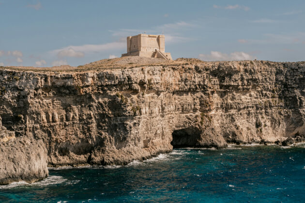 Historischer Santa Maria Tower auf Comino über steiler Kalksteinküste mit Blick auf das Mittelmeer bei klarem Himmel. | Gebeco