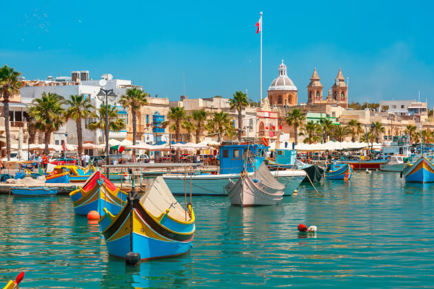Traditionelle bunte Luzzu-Boote im Hafen von Marsaxlokk auf Malta vor historischer Kulisse. | Gebeco