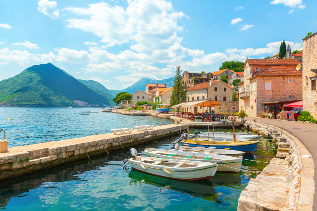 Fischerboote und Uferpromenade vor der Altstadt von Kotor mit Blick auf die Bucht und umliegende Berge. | Gebeco