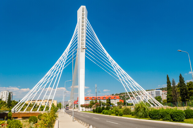 Millennium-Brücke in Podgorica mit weißer Seilstruktur und modernem Stadtbild bei blauem Himmel. | Gebeco