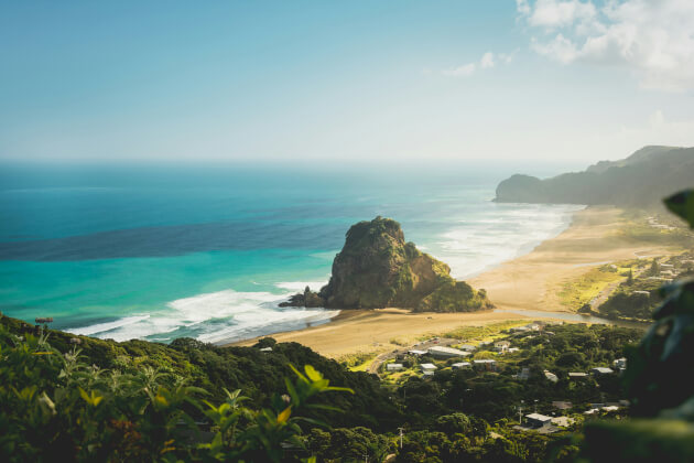 Piha Beach bei Auckland – dramatische Küstenlandschaft mit schwarzem Vulkansand und markantem Felsen im Sonnenlicht. | Gebeco