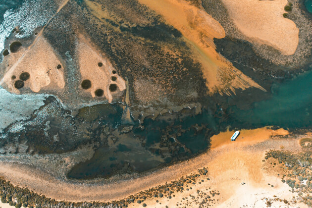 Luftaufnahme des Naturparks Ria Formosa in Faro mit Gezeitenlandschaft, Sandbänken und einem einsamen Boot. | Gebeco