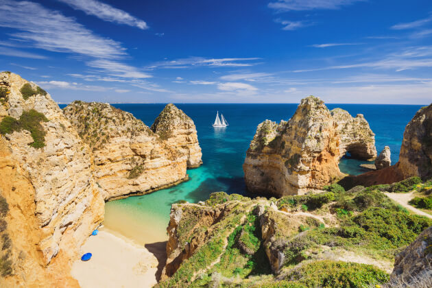 Strand bei Lagos an der Algarve mit Felsformationen, türkisfarbenem Wasser und Segelboot. | Gebeco