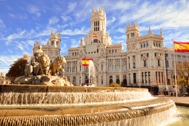 Plaza de Cibeles mit Neptunbrunnen und Palacio de Cibeles in Madrid bei blauem Himmel und spanischen Flaggen. | Gebeco