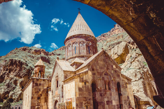 Geghard-Kloster in Armenien mit spitzem Kuppeldach, eingebettet in eine Felsenschlucht bei blauem Himmel. | Gebeco