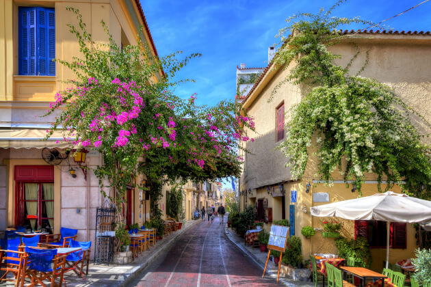 Blumengeschmückte Gasse im Athener Altstadtviertel Plaka mit Tavernen und bunten Häusern bei Sonnenschein. | Gebeco