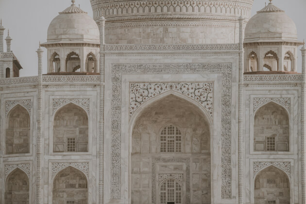 Detailansicht der kunstvoll verzierten Fassade des Taj Mahals in Agra, Indien – mit symmetrischen Bögen, Marmorornamenten und filigraner Architektur. | Gebeco