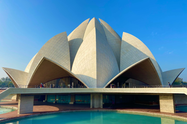 Außenansicht des Lotus-Tempels in Delhi bei blauem Himmel, spiegelnd im umliegenden Wasserbecken. | Gebeco