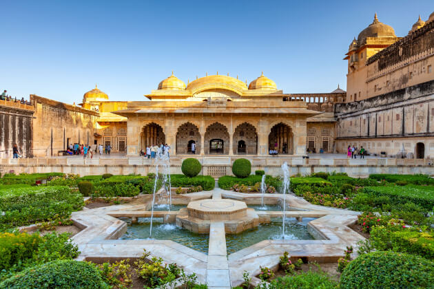 Blick auf den kunstvollen Gartenhof des Amber Forts in Jaipur mit Wasserfontänen und Palastarkaden im Hintergrund. | Gebeco