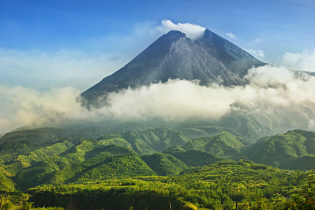 Blick auf den mächtigen Vulkan Merapi auf Java, umgeben von grüner Hügellandschaft und aufsteigendem Nebel. | Gebeco