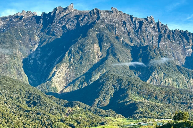 Blick auf den majestätischen Mount Kinabalu auf Borneo in Malaysia mit grünem Tal im Vordergrund und steiler Felswand im Hintergrund. | Gebeco