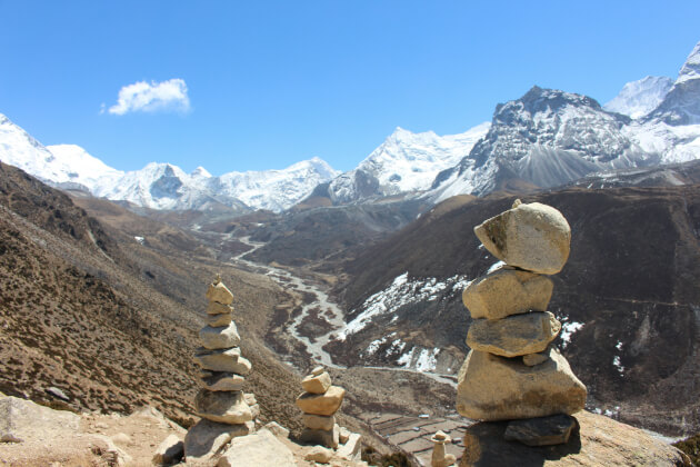 Steinmännchen im Vordergrund vor einem weiten Himalaya-Tal mit schneebedeckten Gipfeln unter klarem Himmel. | Gebeco