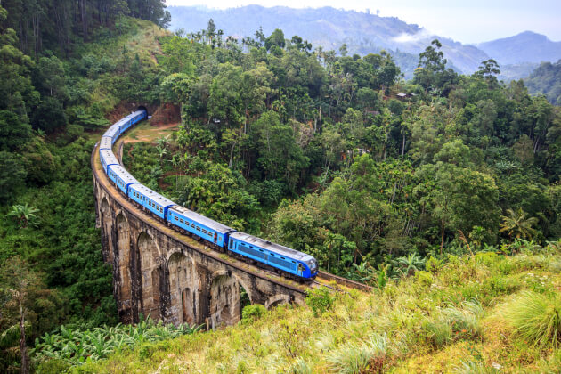 Blauer Zug überquert die historische Nine Arches Bridge inmitten grüner Hügel bei Ella, Sri Lanka. | Gebeco