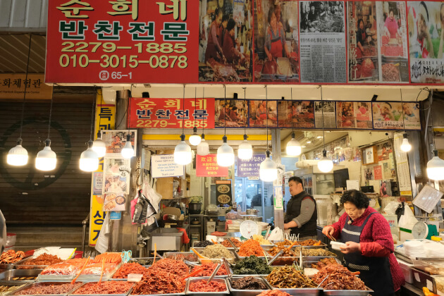 Frau vor einem Essensstand am Seomun-Markt in Daegu, Südkorea, mit einer Vielzahl an eingelegten Speisen. | Gebeco