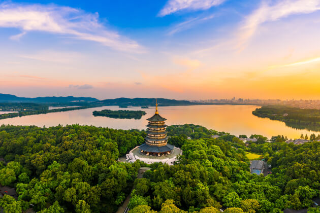 Leifeng-Pagode in Hangzhou vor dem Westsee bei Sonnenuntergang, umgeben von grüner Vegetation