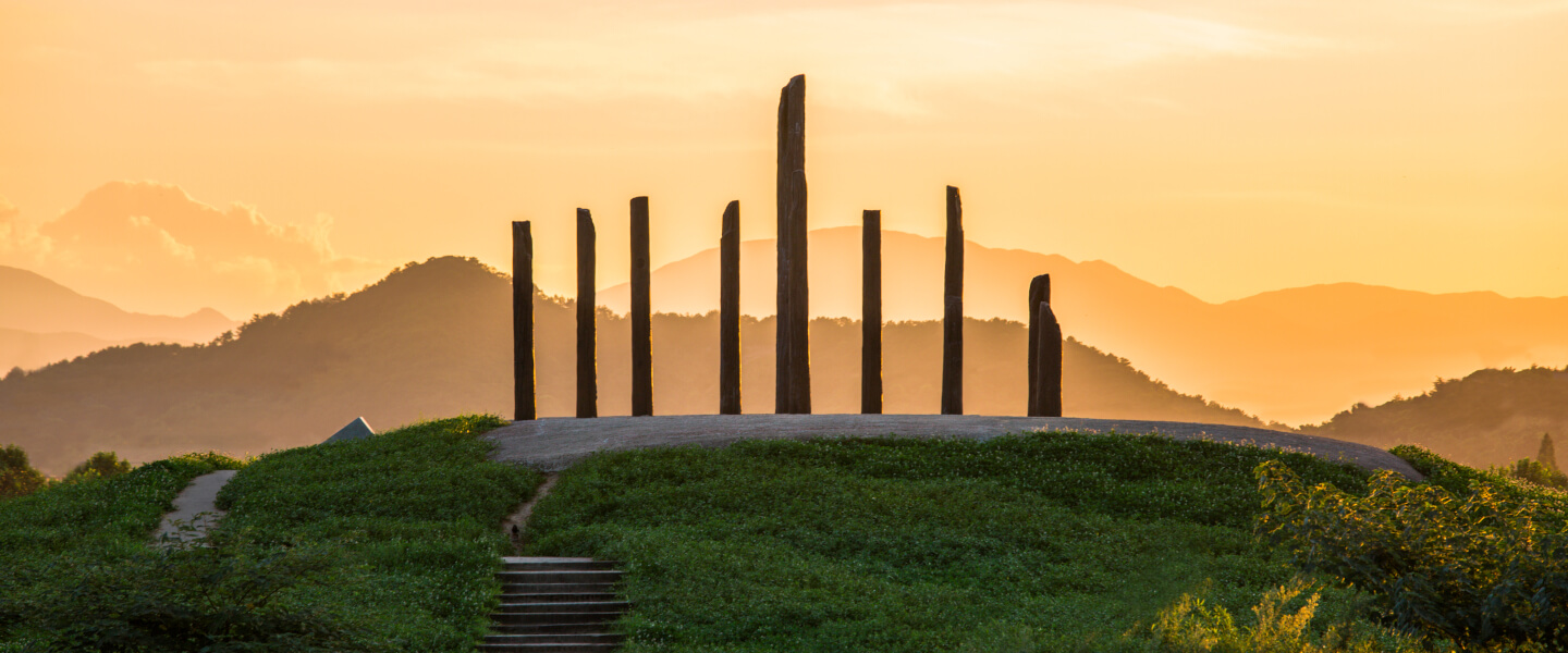 Steinskulptur mit stehenden Monolithen auf Hügel im Sonnenuntergang vor Bergkulisse, Natur und Kunstinstallation in China.