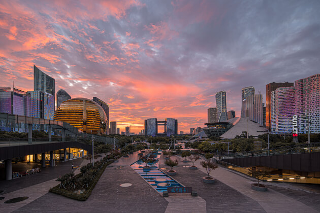 Moderne Skyline von Hangzhou mit goldenem kugelförmigen Konferenzzentrum, auffälligen Hochhäusern und breiter Fußgängerzone bei Sonnenuntergang