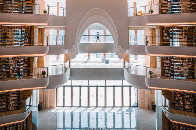 Moderne, lichtdurchflutete Bibliothek in China mit mehreren Etagen, geschwungenen Galerien, zahlreichen Bücherregalen und einer Person auf einer Brücke im Obergeschoss