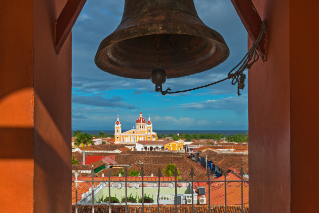 Blick durch eine Kirchenglocke auf die Kathedrale von Granada in Nicaragua mit Gebäuden aus der Kolonialzeit und blauem Himmel.