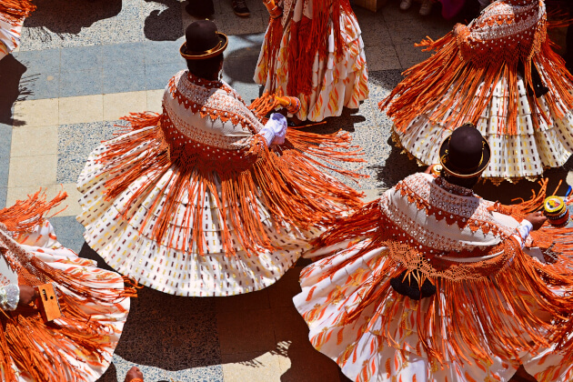 Peruanische Tänzerinnen in traditioneller Kleidung mit weiten, bunten Röcken und Melonenhüten bei einem Straßenfest. | Gebeco