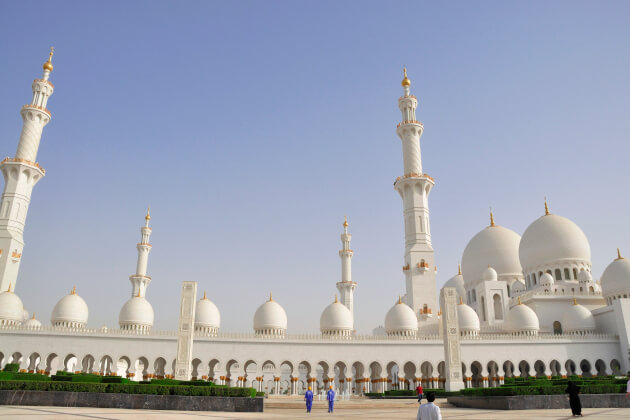 Hof der Scheich-Zayid-Moschee in Abu Dhabi mit weißen Kuppeln und Minarett unter blauem Himmel. | Gebeco