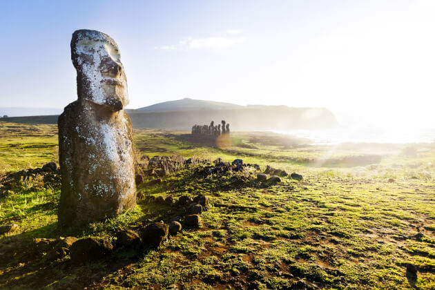 Moai-Steinfigur auf der Osterinsel bei Sonnenaufgang mit weiteren Statuen im Hintergrund. | Gebeco