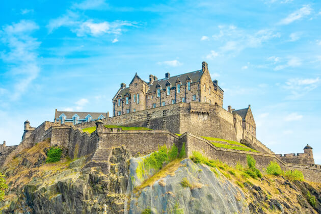 Blick auf das Edinburgh Castle auf dem Castle Rock über der Stadt, umgeben von grünen Bäumen und blauer Himmel. | Gebeco