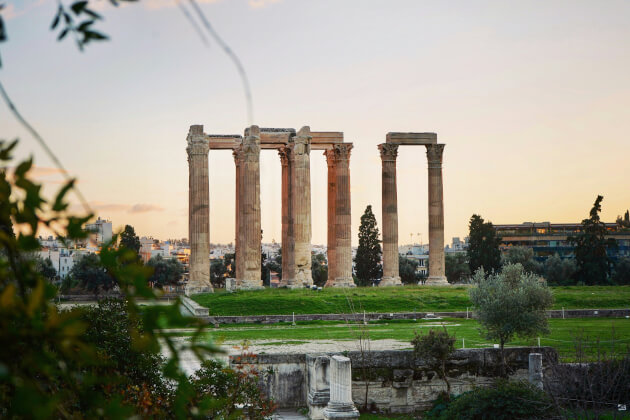 Säulenreste des Zeustempels in Athen bei Sonnenuntergang mit Blick auf grüne Wiesen und die Stadt im Hintergrund. | Gebeco
