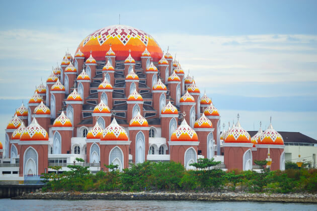 Die farbenfrohe 99-Kuppel-Moschee am Ufer von Makassar, Indonesien, spiegelt sich im ruhigen Wasser. | Gebeco