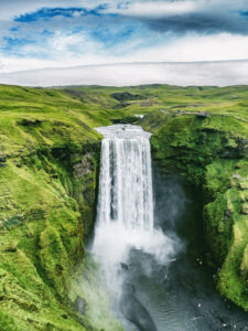 Der breite Skógafoss stürzt imposant in die Tiefe, umgeben von sattgrüner Hügellandschaft. | Gebeco