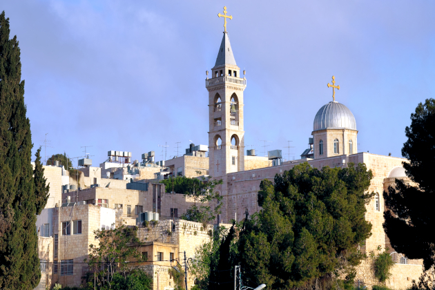 Christliche Kirche mit Glockenturm und silberner Kuppel, beide mit goldenen Kreuzen, in Bethlehem, Nahost, umgeben von Bäumen und städtischer Bebauung.