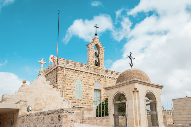 Historische Kirche mit Glockenturm und Steinfassade, mehreren Kreuzen und Kuppel, unter blauem Himmel in Bethlehem, Nahost.